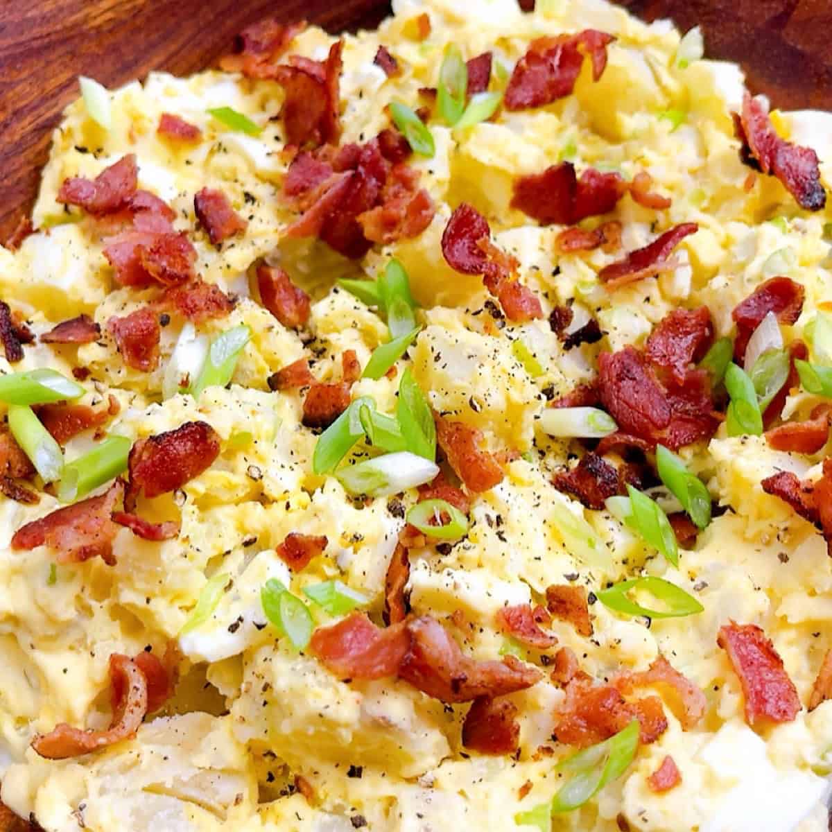 Southern potato salad with bacon and green onion garnish in a wooden bowl.