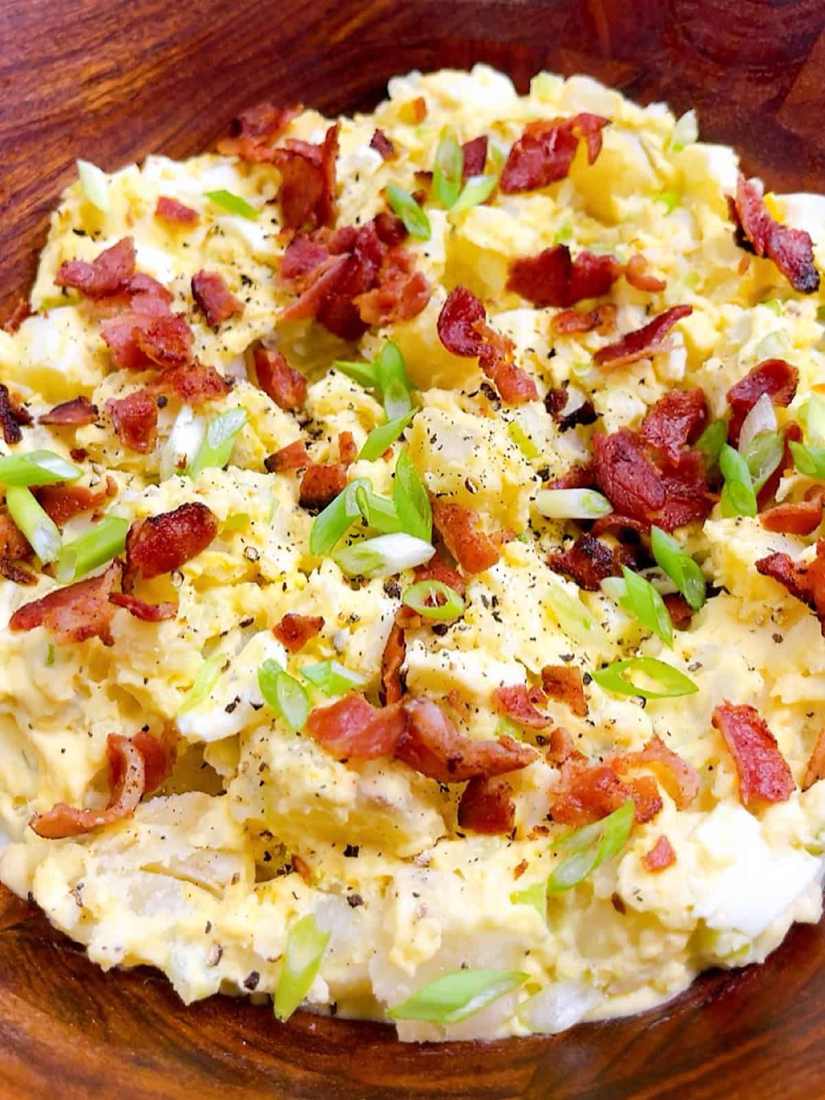 Southern potato salad with bacon and green onion garnish in a wooden bowl.
