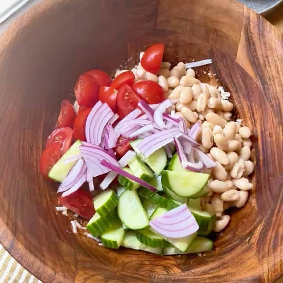 A wooden salad bowl with all ingredients for the white bean salad except basil.