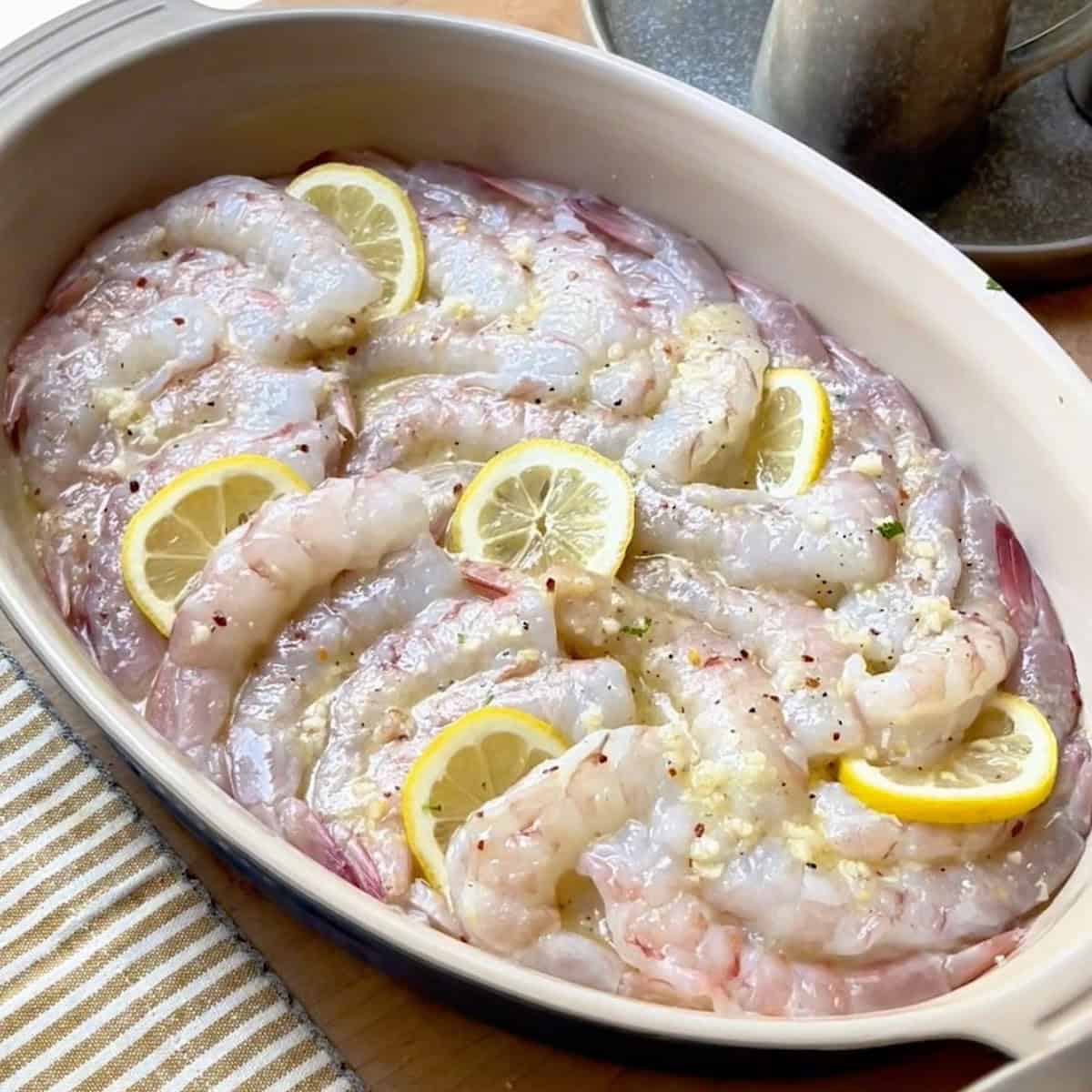 Shrimp arranged in oval baking dish with lemon tucked between.
