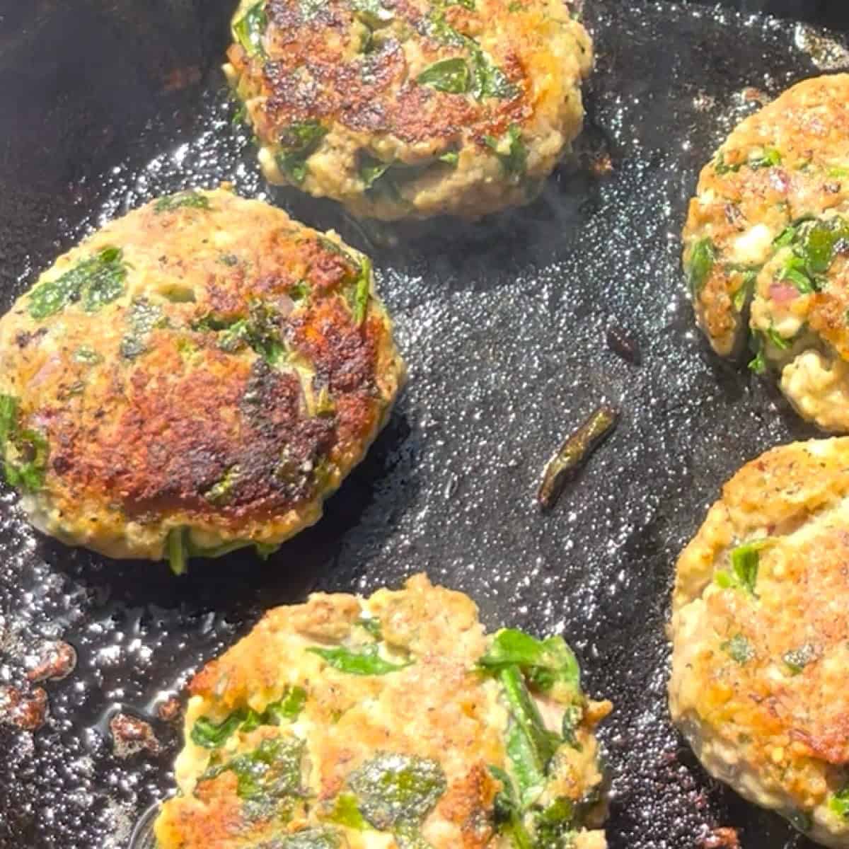 Spinach and feta turkey burgers searing in a cast iron skillet.