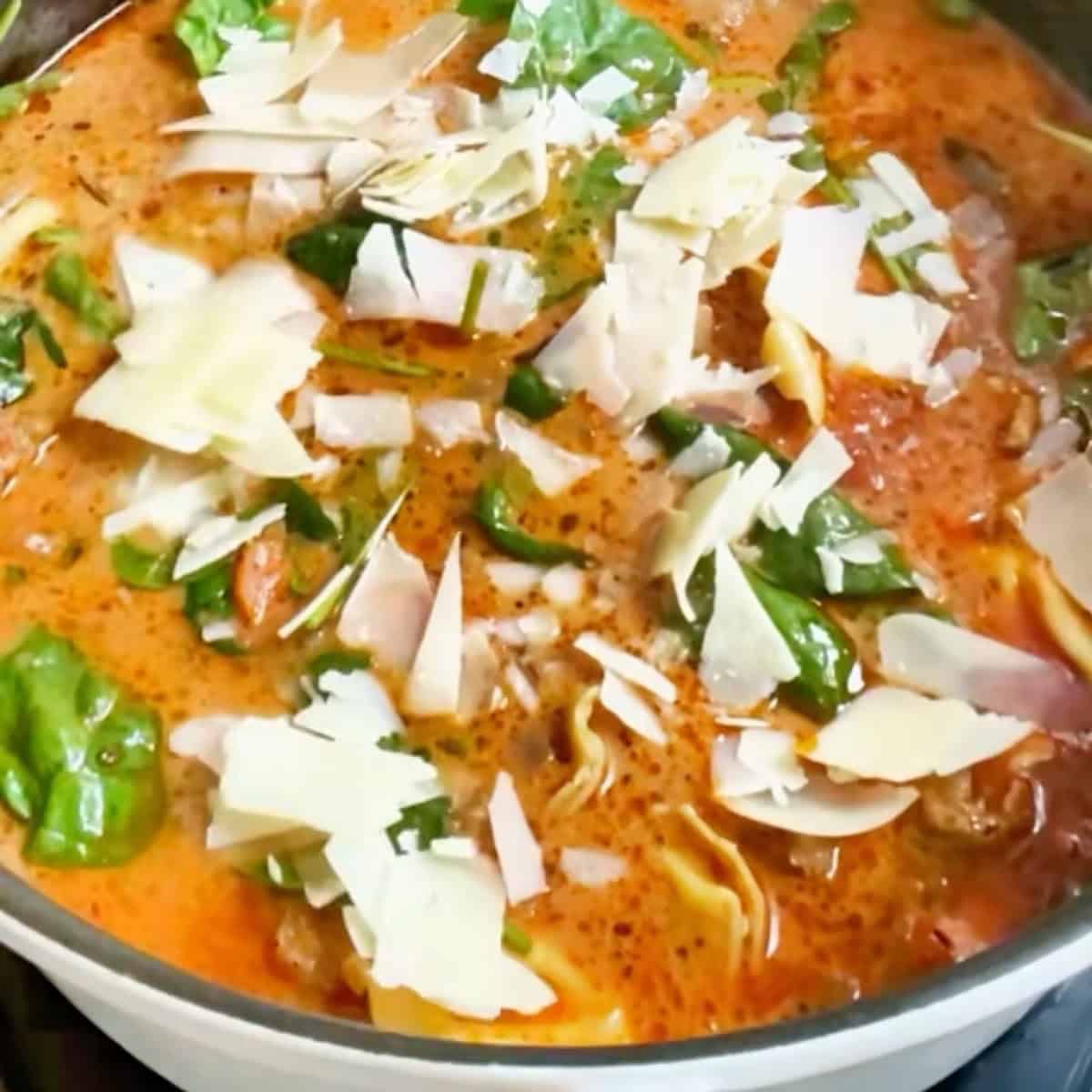 Creamy Tuscan Tortellini Soup in white Staub dutch oven with shaved parmesan on top.
