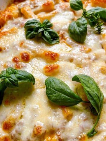 Baked ziti with ground beef in a casserole dish with fresh basil leaves on top.
