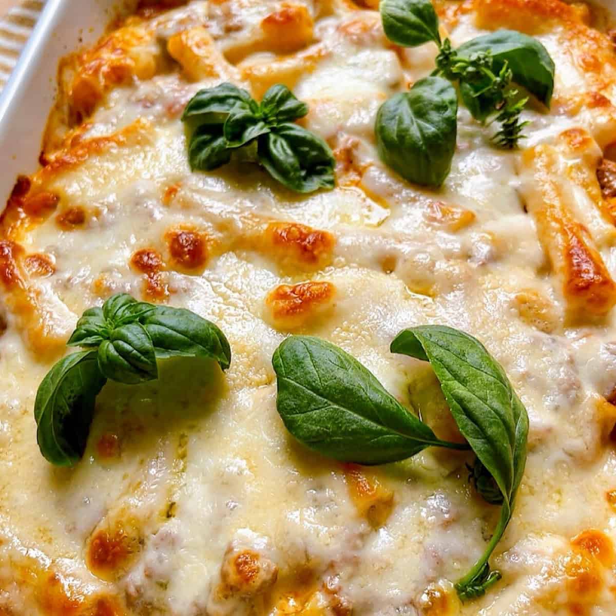 Baked ziti with ground beef in a casserole dish with fresh basil leaves on top.