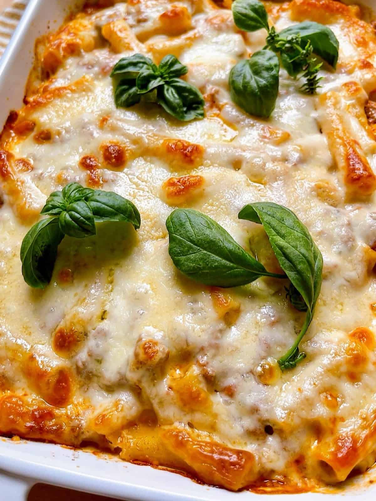 Baked ziti with ground beef in a casserole dish with fresh basil leaves on top.