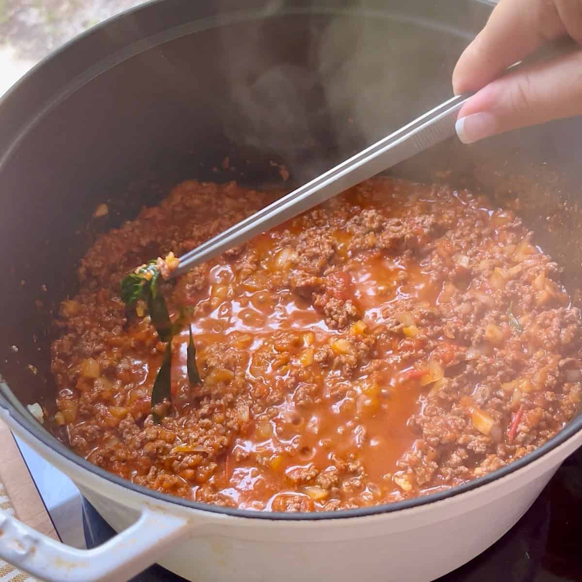 Removing fresh basil from beef marinara sauce.