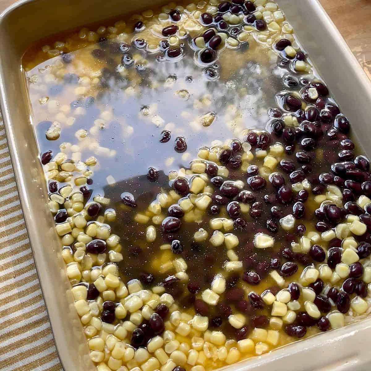 Prepared rice base with corn, black beans, and broth in a casserole dish.