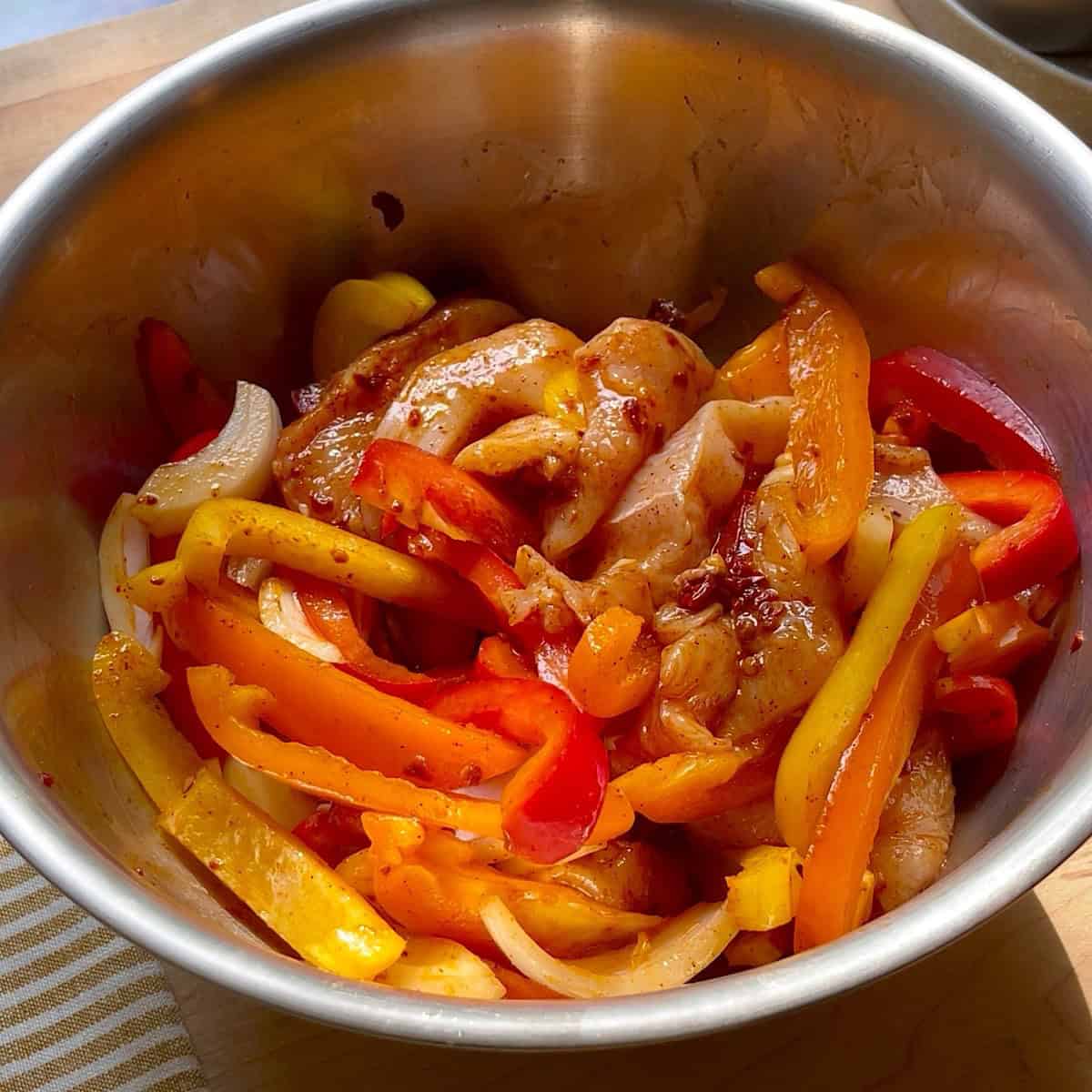 Chicken, peppers, and onion tossed in a bowl with fajita and chipotle seasoning.