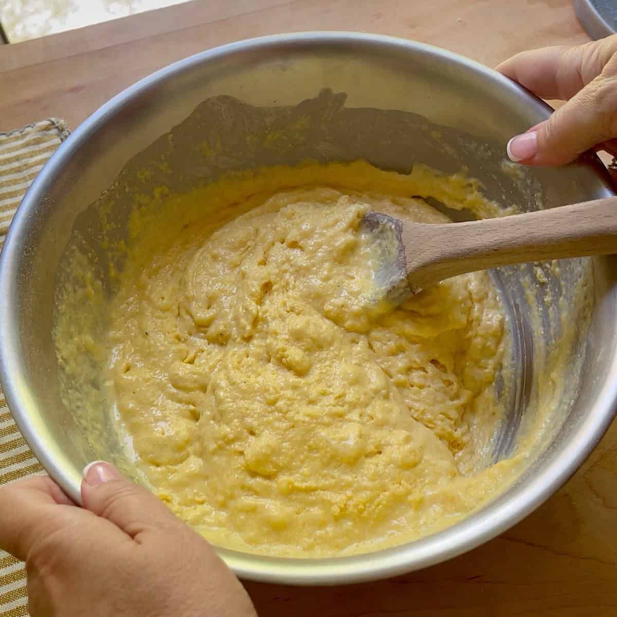 Wet and dry ingredients mixed together in a mixing bowl with wooden spoon.