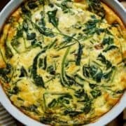 A Mediterranean quiche fully cooked in a white quiche dish.