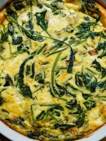 A Mediterranean quiche fully cooked in a white quiche dish.
