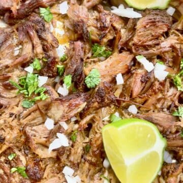 Mexican pulled pork with crispy edges on a sheet pan topped with onion, cilantro, and lime wedges.