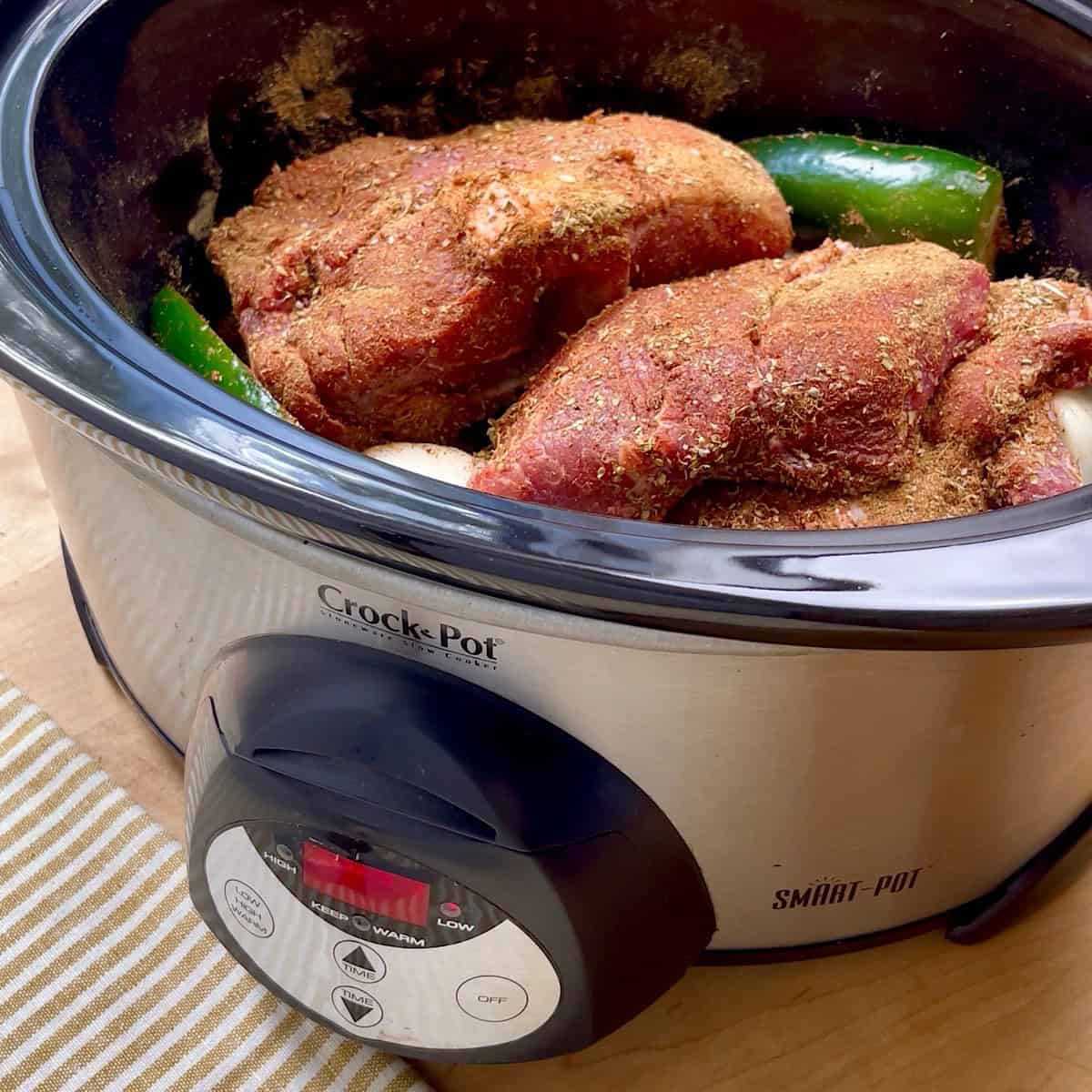 Spice rubbed pork shoulder sitting on top of onion, garlic, and jalapeno in a crockpot.
