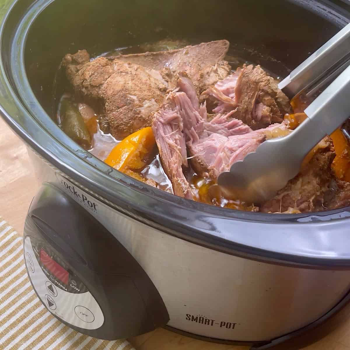 Tongs grabbing the cooked pork to show that it shreds easily.