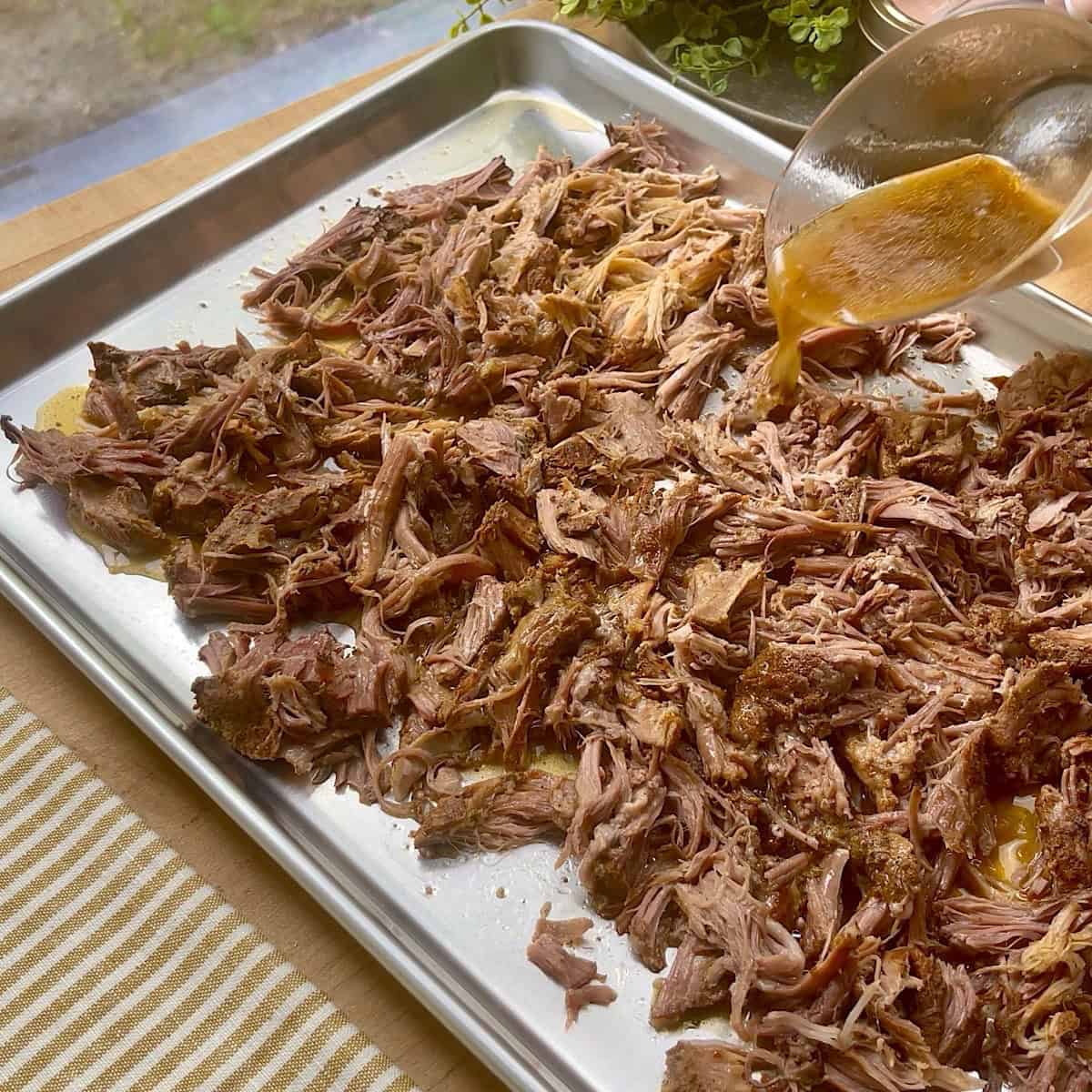 Shredded pork on a sheet pan with juices being poured over top.
