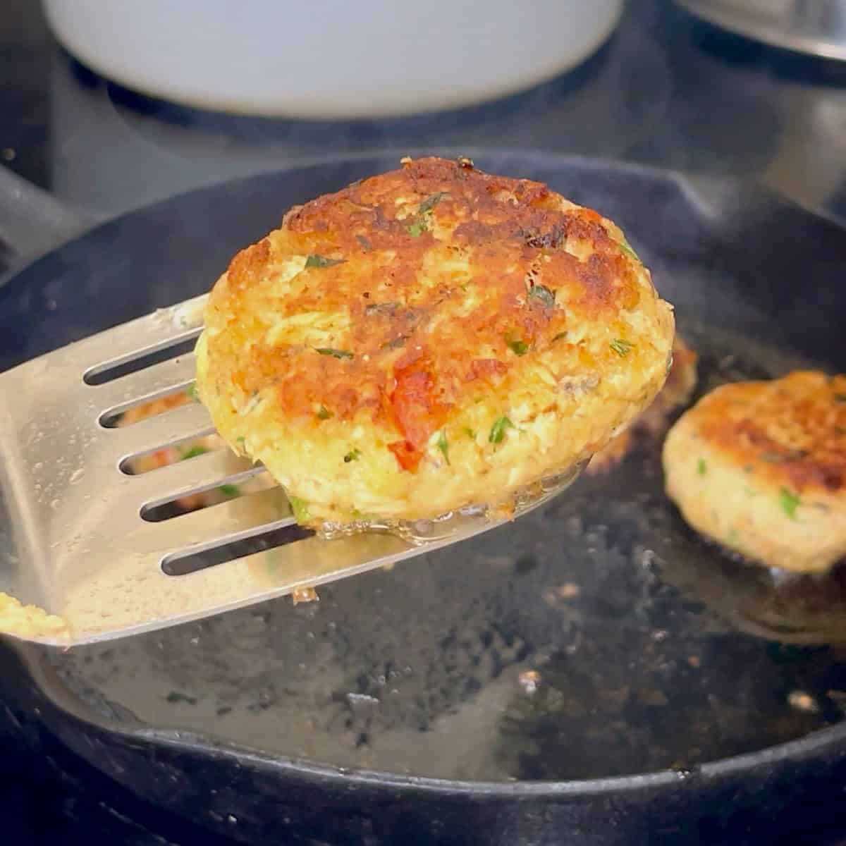 A spatula holding a browned salmon patty over a cast iron skillet.