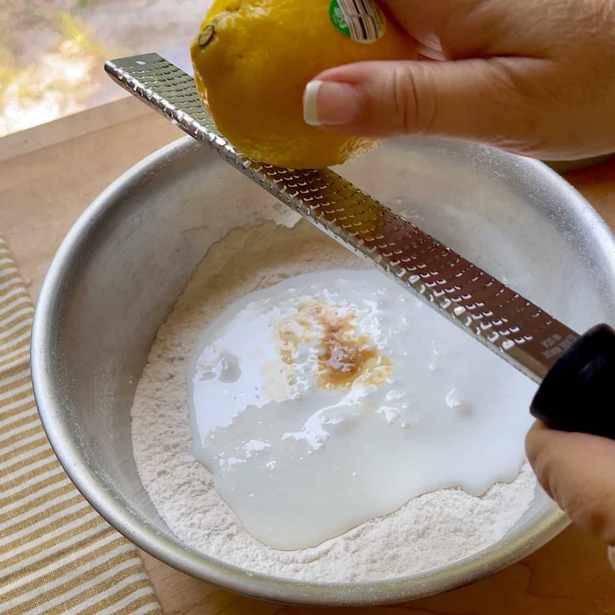 Zesting lemon over sifted dough ingredients and buttermilk.