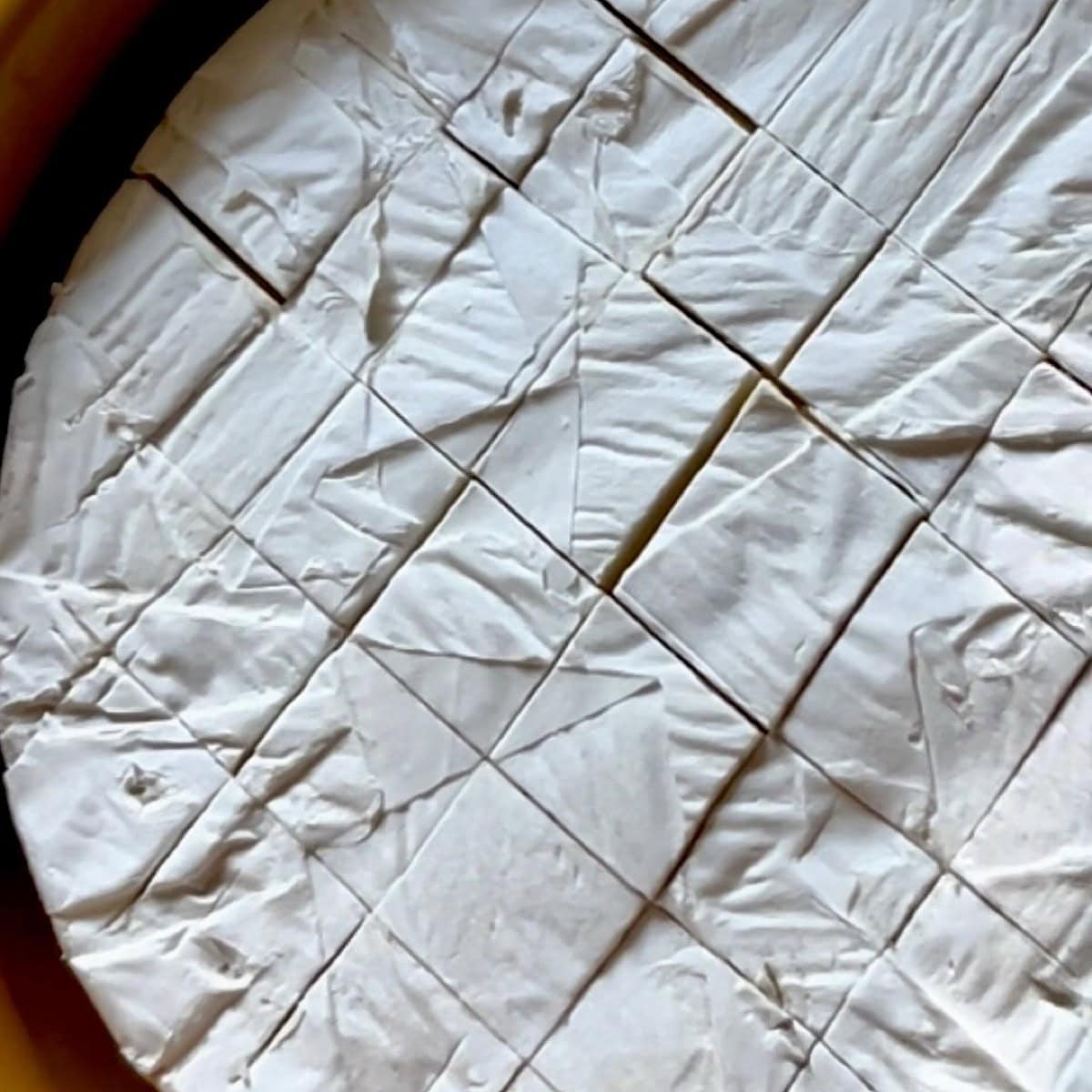Brie cheese scored with crosshatch pattern.