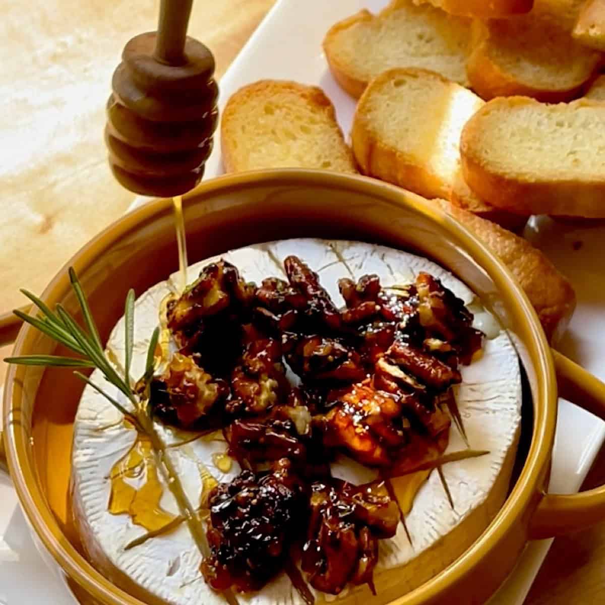 Dripping honey on brie cheese with fig jam, rosemary, and pecan topping.