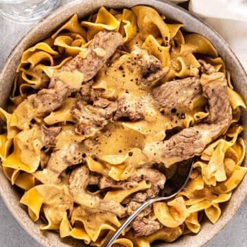 A bowl of beef stroganoff with a spoon inside and a linen napkin nearby.