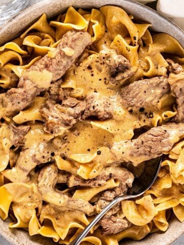 A bowl of beef stroganoff with a spoon inside and a linen napkin nearby.