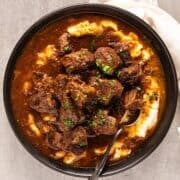 Braised beef tips recipe in a bowl over mashed potatoes.