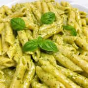 Creamy pesto pasta in a white bowl with fresh basil leaves on top.