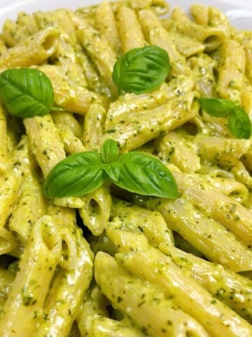 Creamy pesto pasta in a white bowl with fresh basil leaves on top.