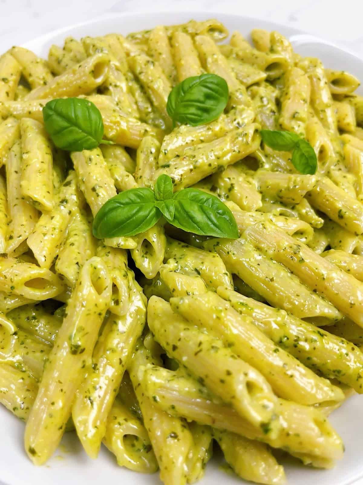 Creamy pesto pasta in a white bowl with fresh basil leaves on top.