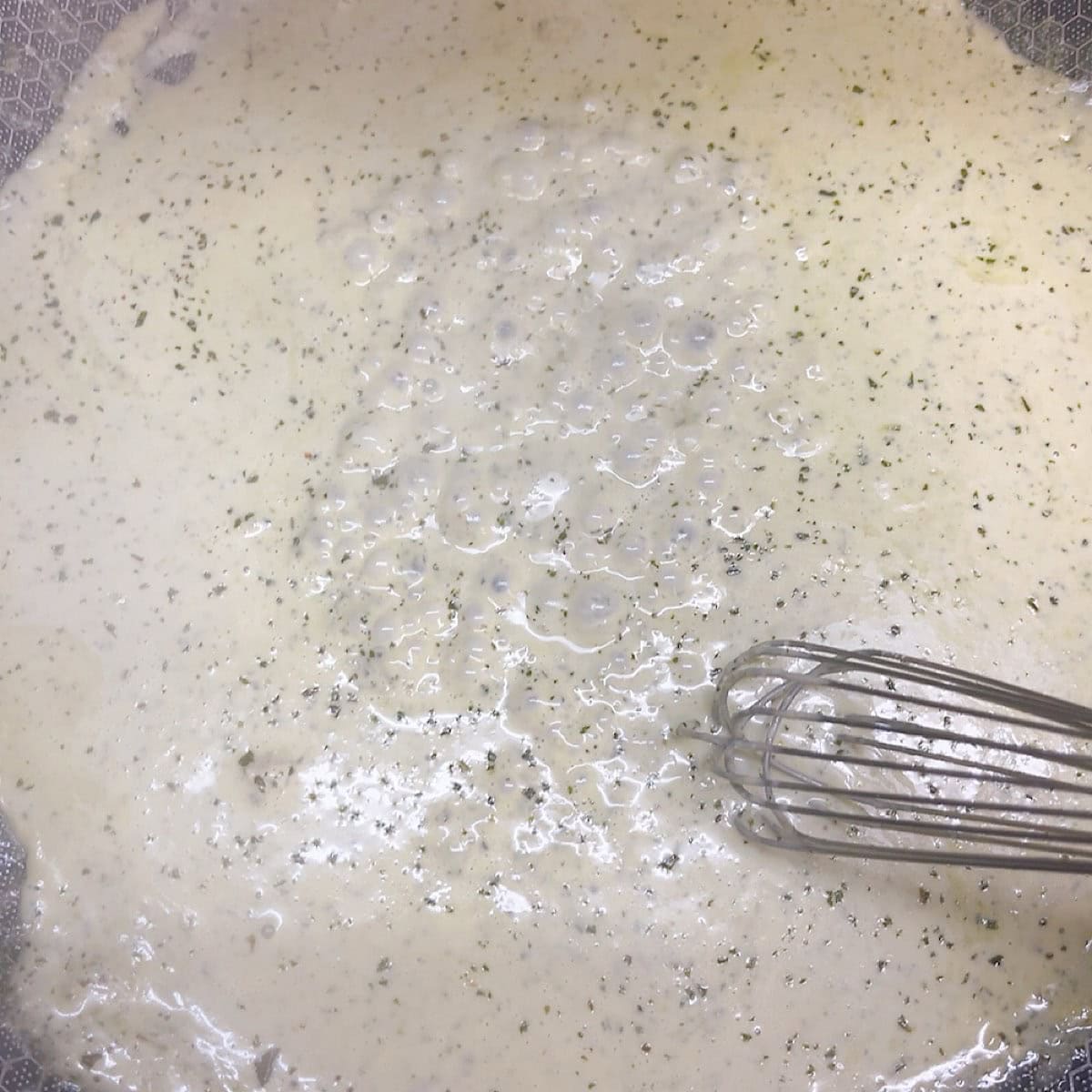 Whisking the creamy pesto sauce in a pan.