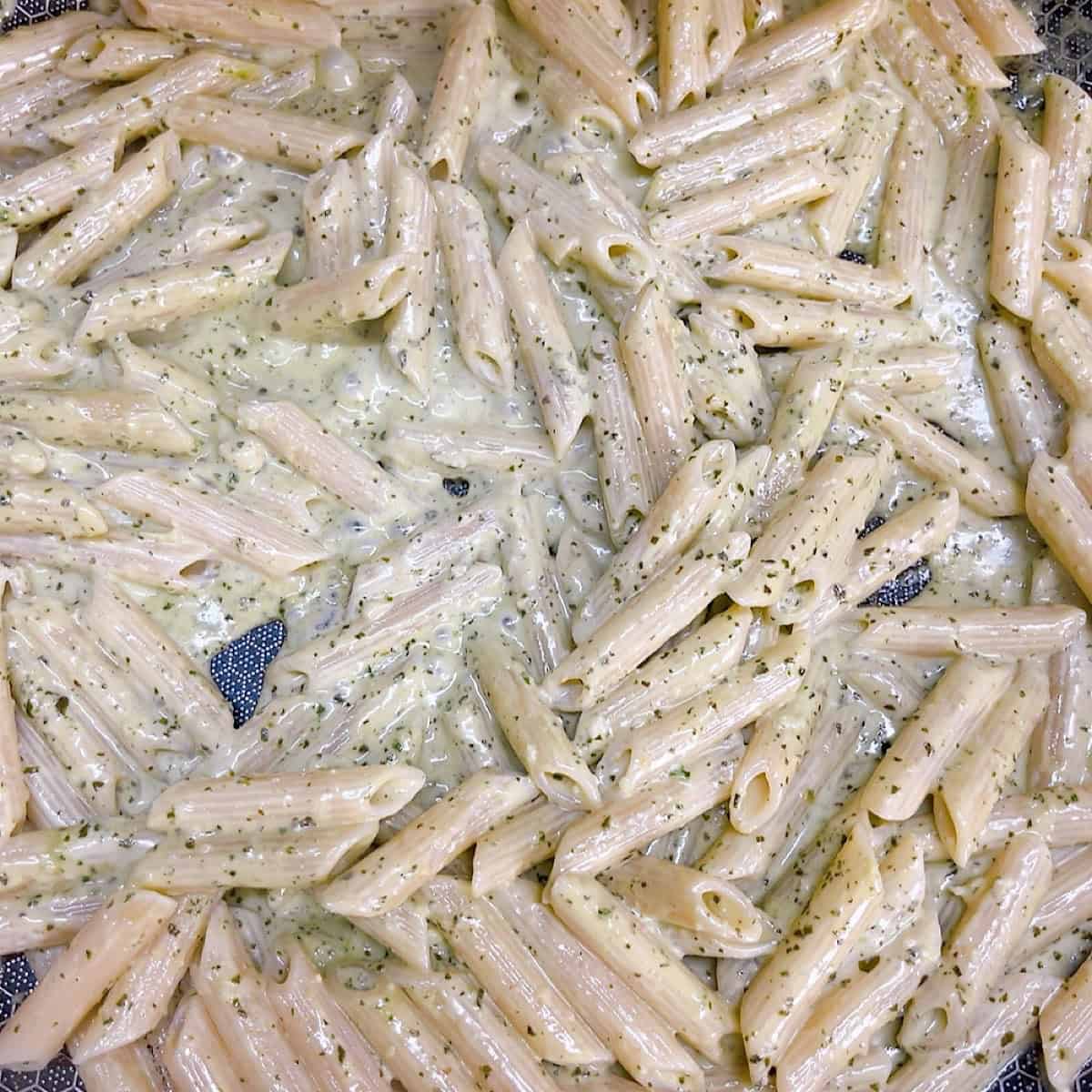 Combining the pesto with ziti pasta.