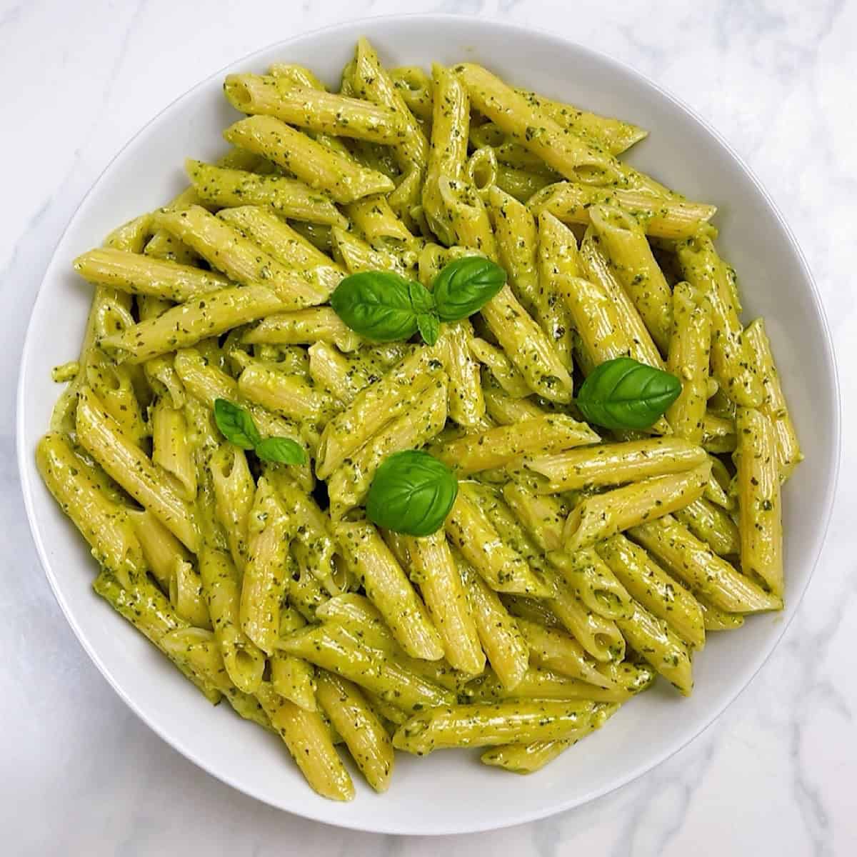 Creamy pesto pasta in a white bowl with fresh basil on top ready to serve.