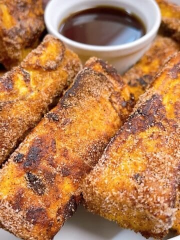 Cinnamon Sugar Brioche French toast sticks in a platter with maple syrup for dipping.