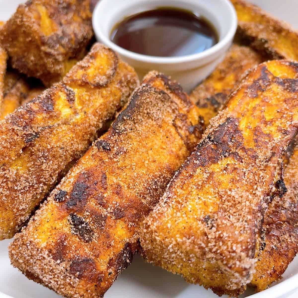 Cinnamon Sugar Brioche French toast sticks in a platter with maple syrup for dipping.