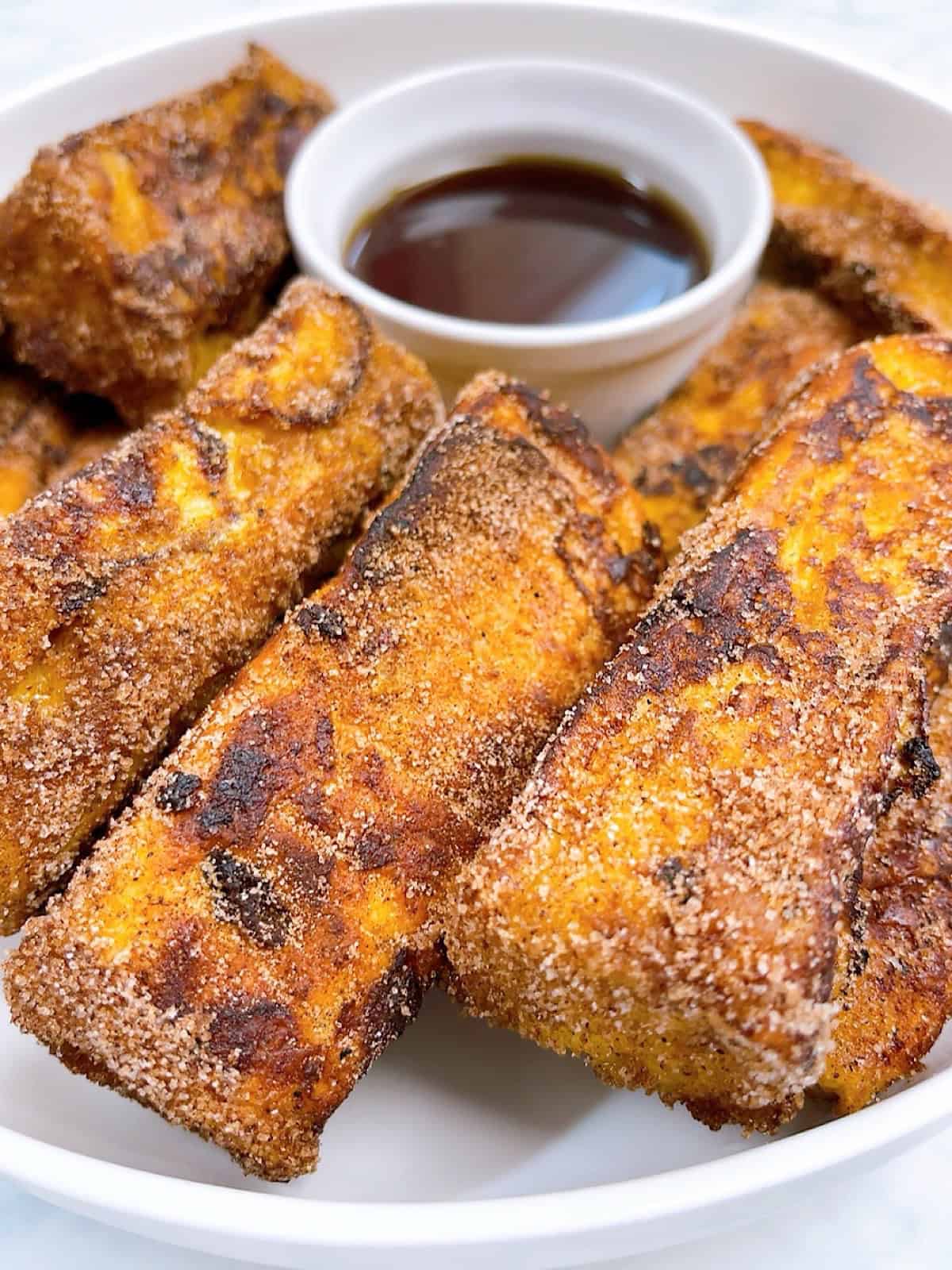 Cinnamon Sugar Brioche French toast sticks in a platter with maple syrup for dipping.