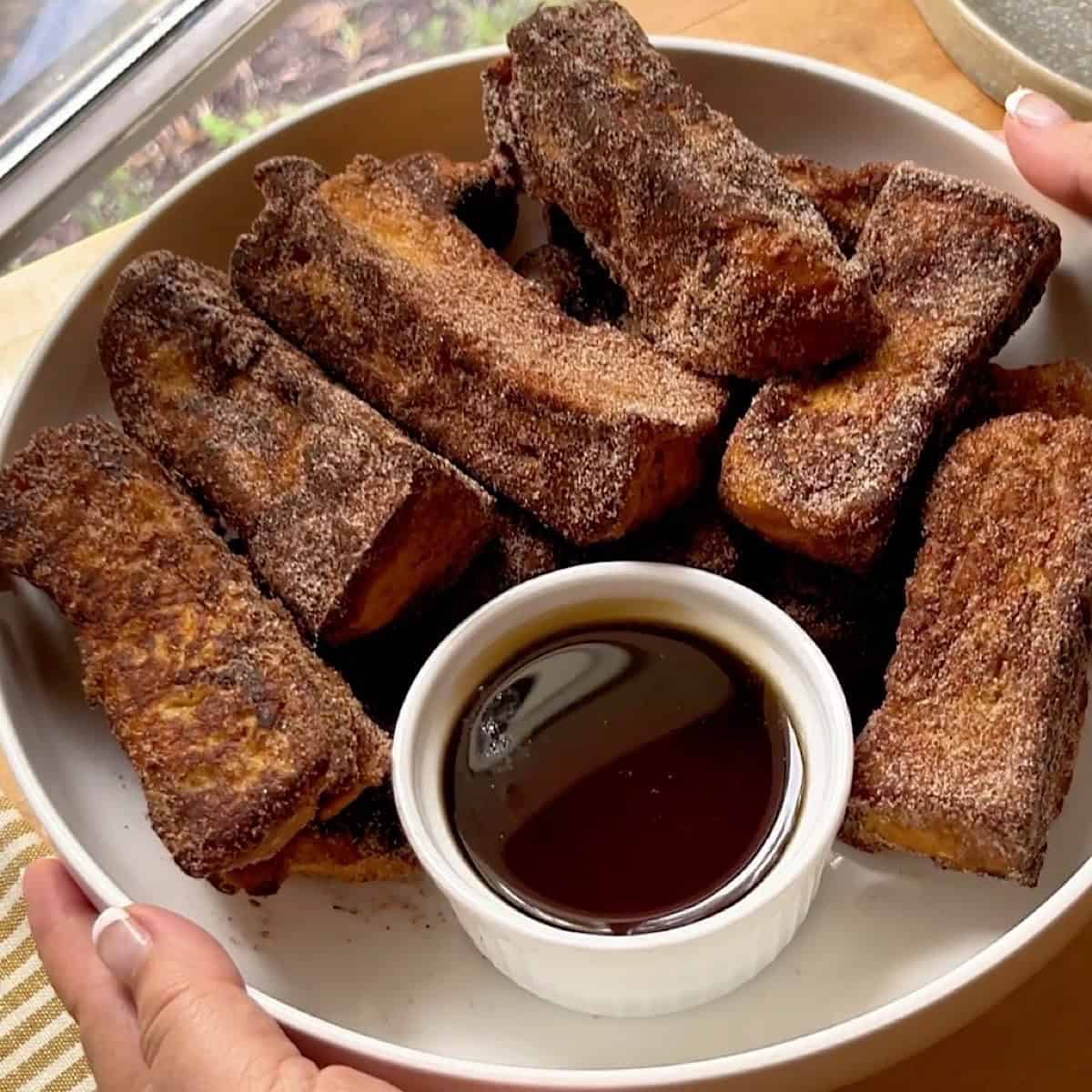 Cinnamon sugar French toast sticks in a serving platter with maple syrup.