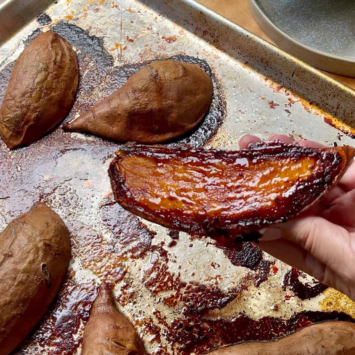 A caramelized sweet potato being held in my hand over a baking sheet.