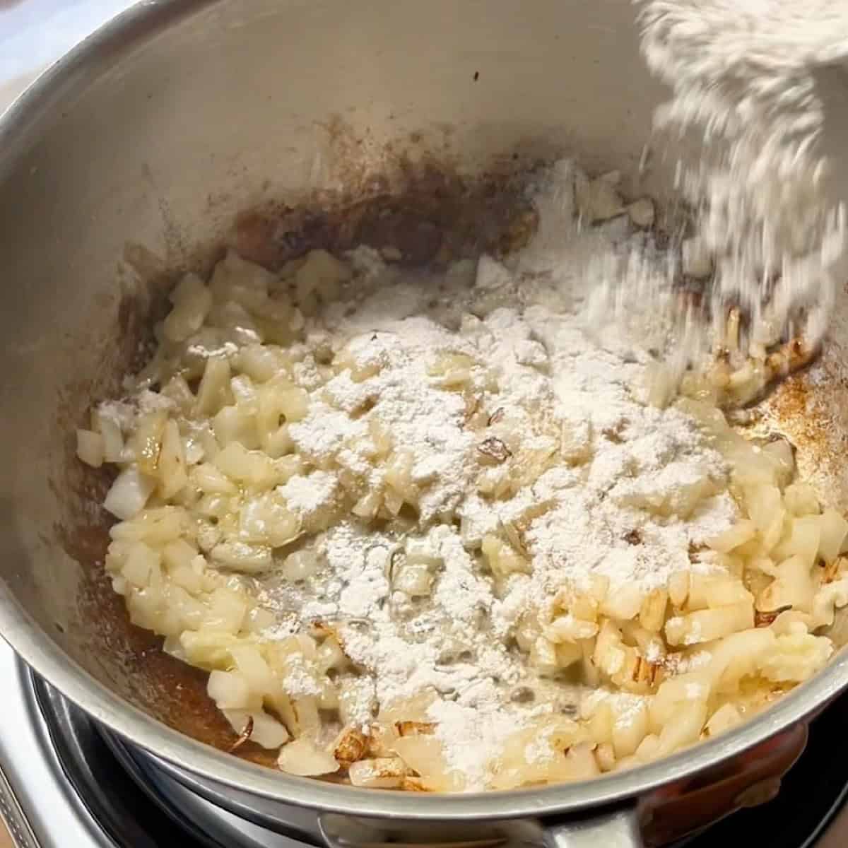 Sprinkling flour over onion, garlic, and butter to make a roux.