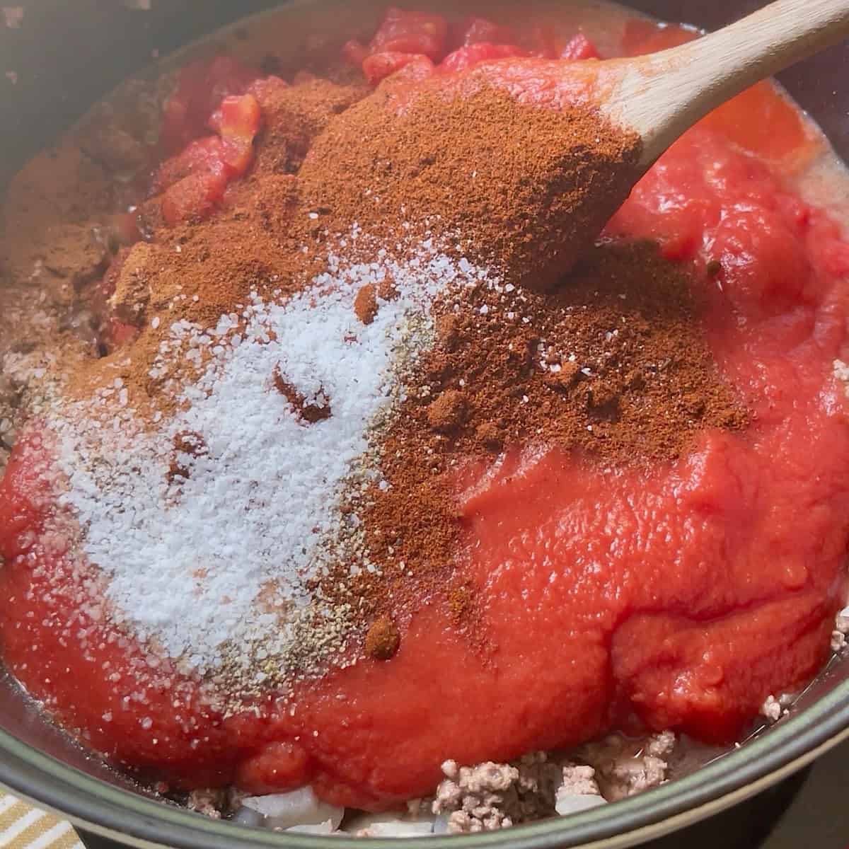 Adding tomatoes and spices to the ground beef.