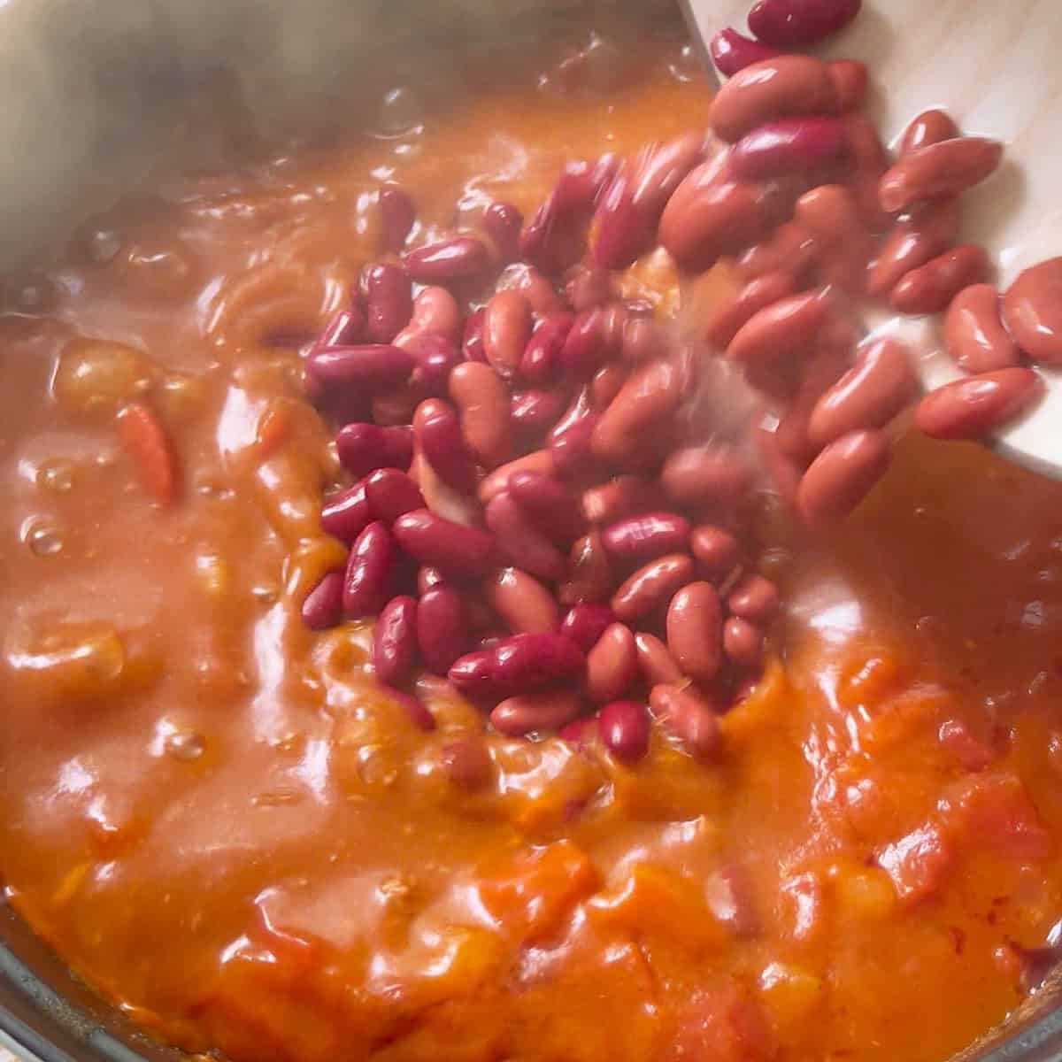 Adding kidney beans to the chili with vinegar.