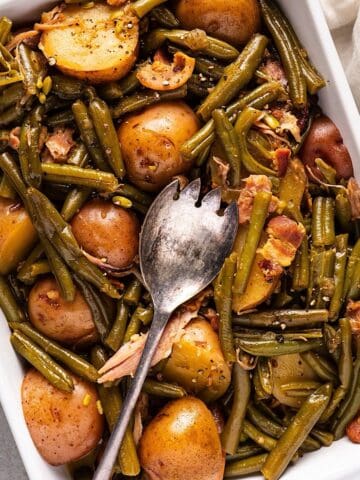 Green beans and new potatoes in a casserole dish with a serving utensil.