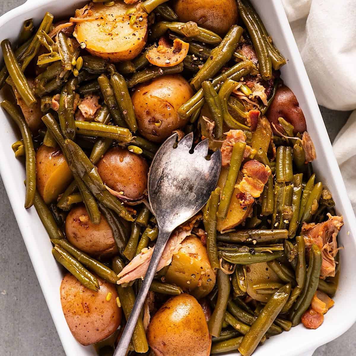 Green beans and new potatoes in a casserole dish with a serving utensil.