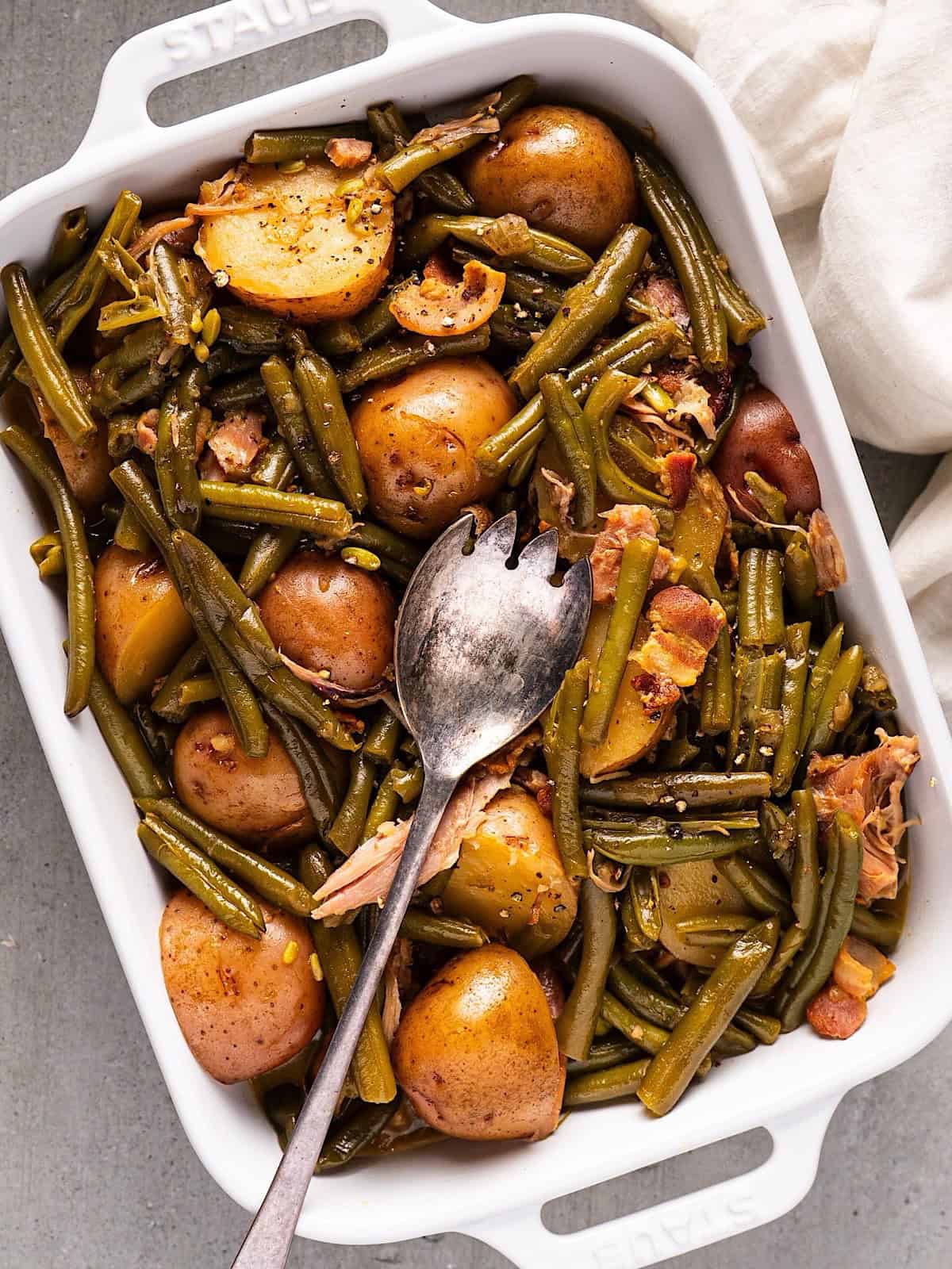 Green beans and new potatoes in a casserole dish with a serving utensil.