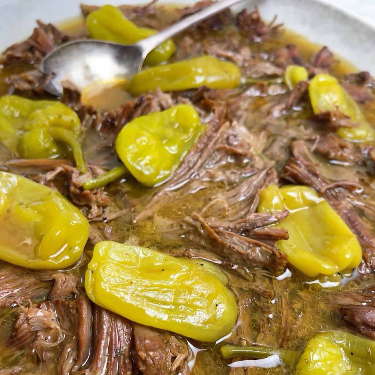 Mississippi pot roast in a serving dish with juices and the peppers on top.