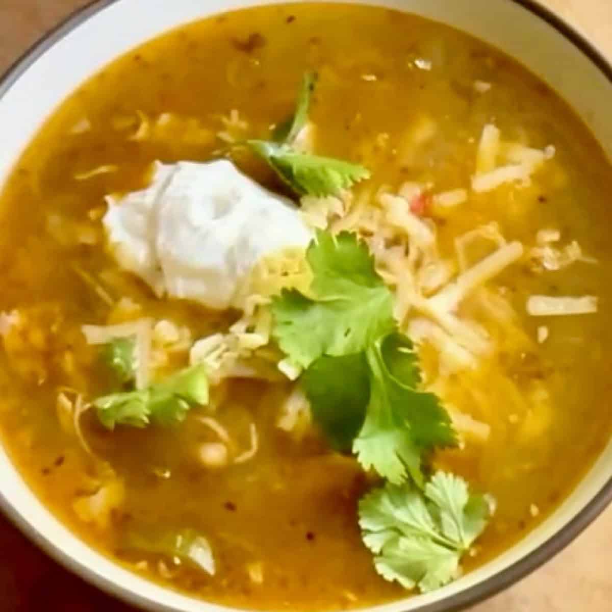 White chicken chili with salsa verde in a bowl with cilantro, cheese, and sour cream topping.