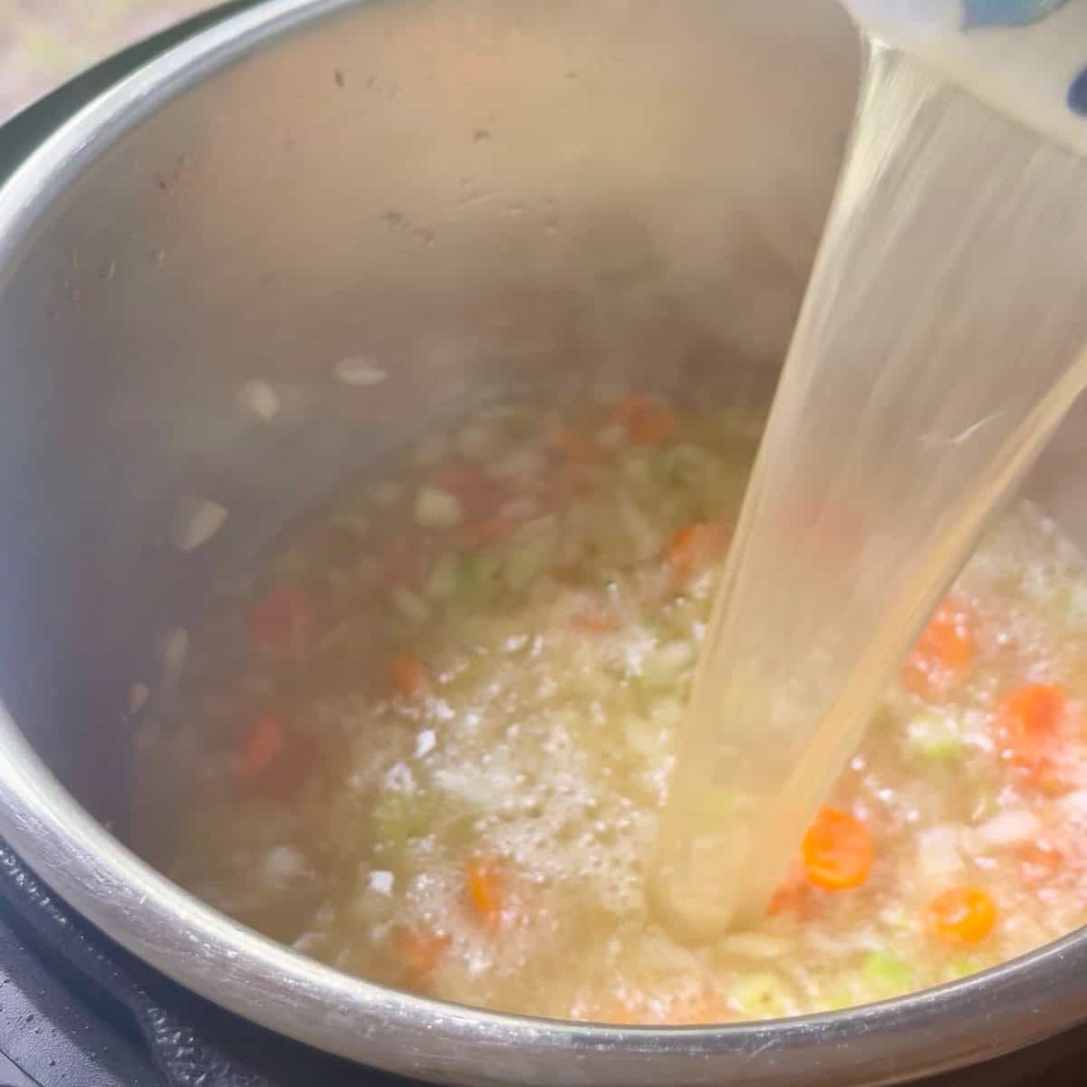 Broth being added to sauteed vegetables.