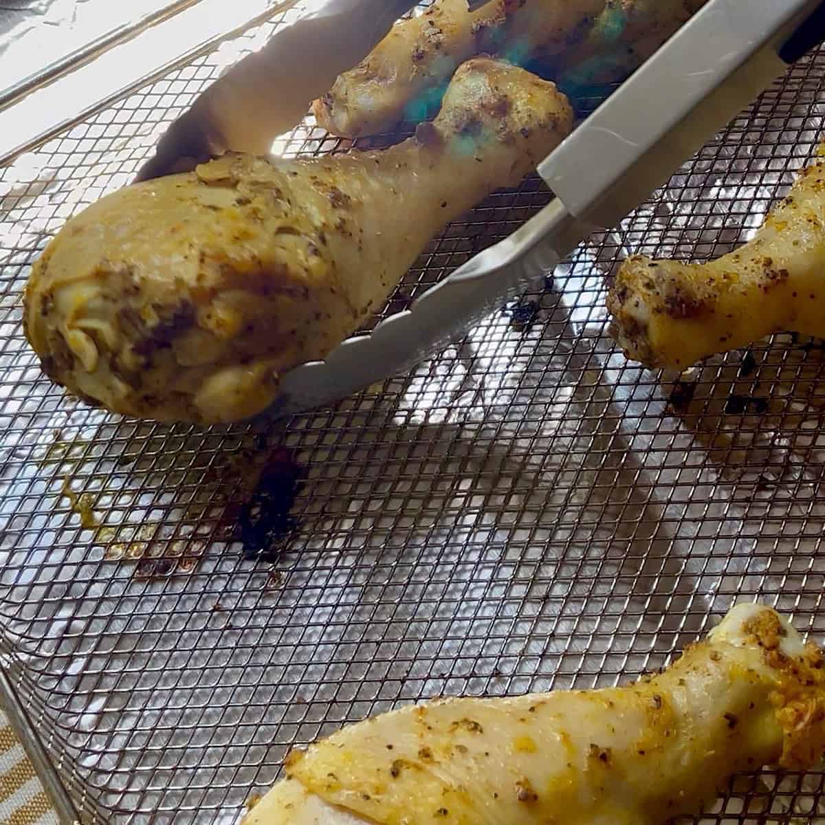 Flipping the lemon pepper chicken legs with tongs.