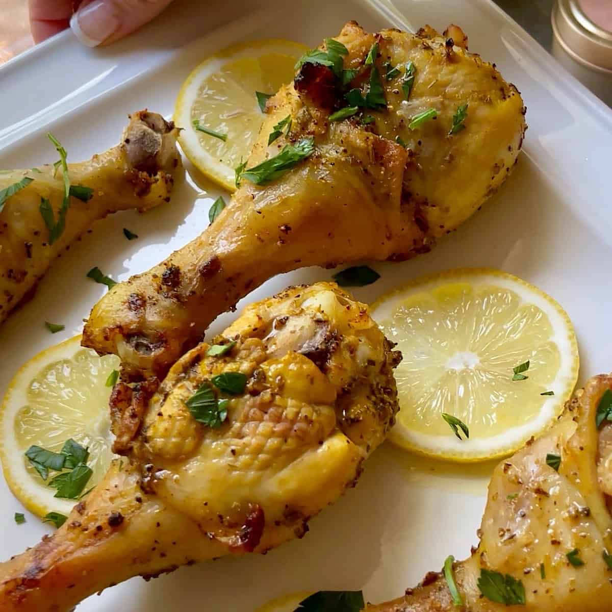 Air fried lemon pepper drumsticks on a platter with lemon and fresh parsley.