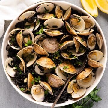 Linguine nero di seppia in serving bowl with garnish and lemon wedges.