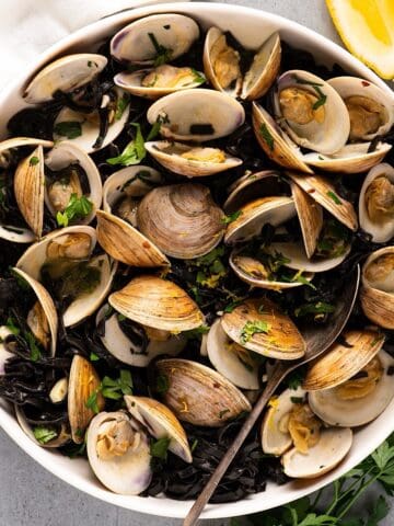 Linguine nero di seppia in serving bowl with garnish and lemon wedges.